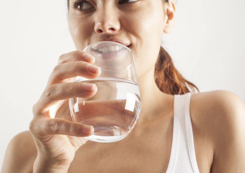 Woman drinking water from a glass, promoting hydration and wellness in health insurance context.