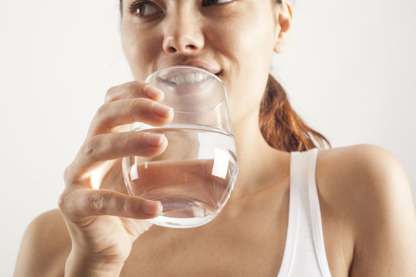 Woman holding a glass of water, promoting hydration and healthy lifestyle choices for improved well-being.