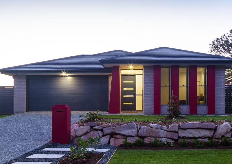 Modern home exterior with red accents, landscaped garden, and driveway, relevant to wellness and aging in place.