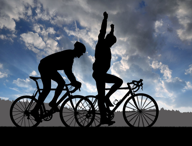 Silhouettes of two cyclists against a dramatic sky, one celebrating with arms raised, symbolizing the mental health benefits of exercise and promoting an active lifestyle.