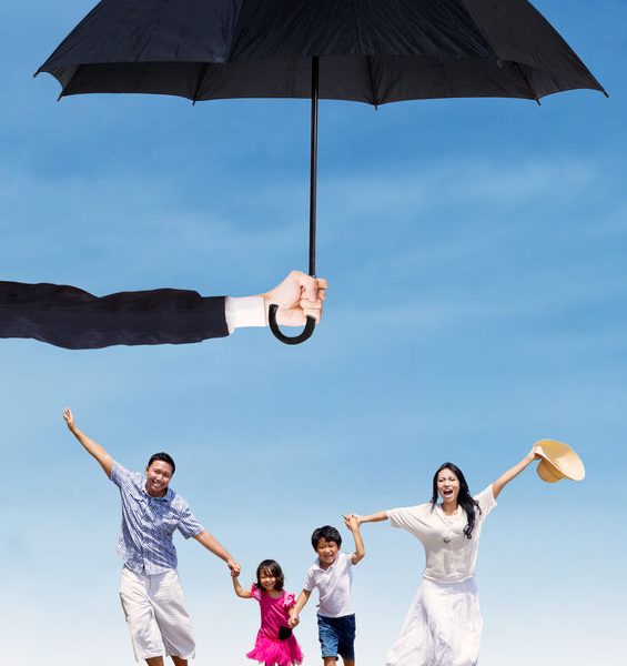 Family enjoying a sunny day outdoors under a large umbrella, symbolizing protection and well-being, relevant to health insurance and wellness discussions.