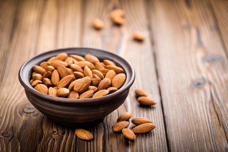 Bowl of almonds on wooden table, representing healthy snack options for improved nutrition and wellness.
