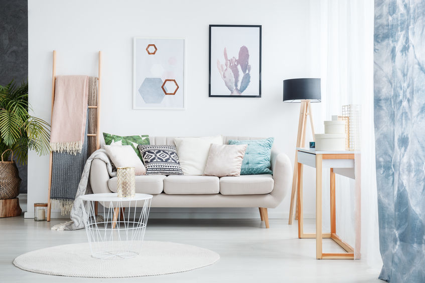 Modern living room with a light-colored sofa adorned with decorative pillows, minimalist artwork on the walls, a round area rug, and a stylish side table featuring decorative items, emphasizing home decor for new homeowners.