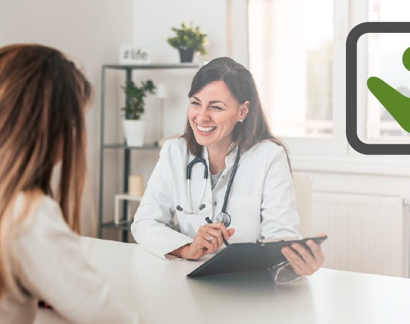 Doctor consulting with a patient, smiling and holding a tablet, in a bright office setting, highlighting health insurance discussions.