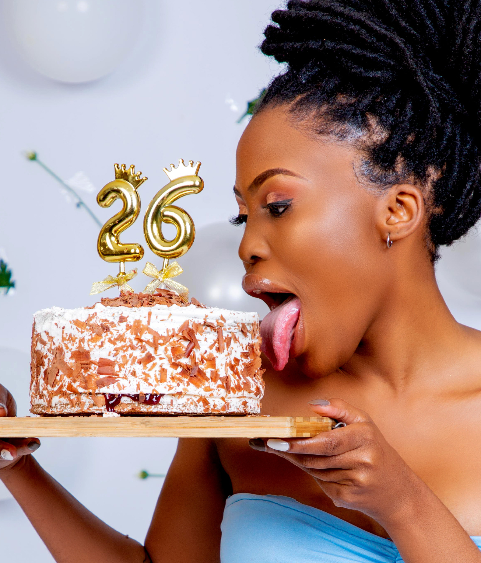 Woman playfully licking a chocolate birthday cake topped with "26" candles, celebrating the transition to independent health insurance options after turning 26.