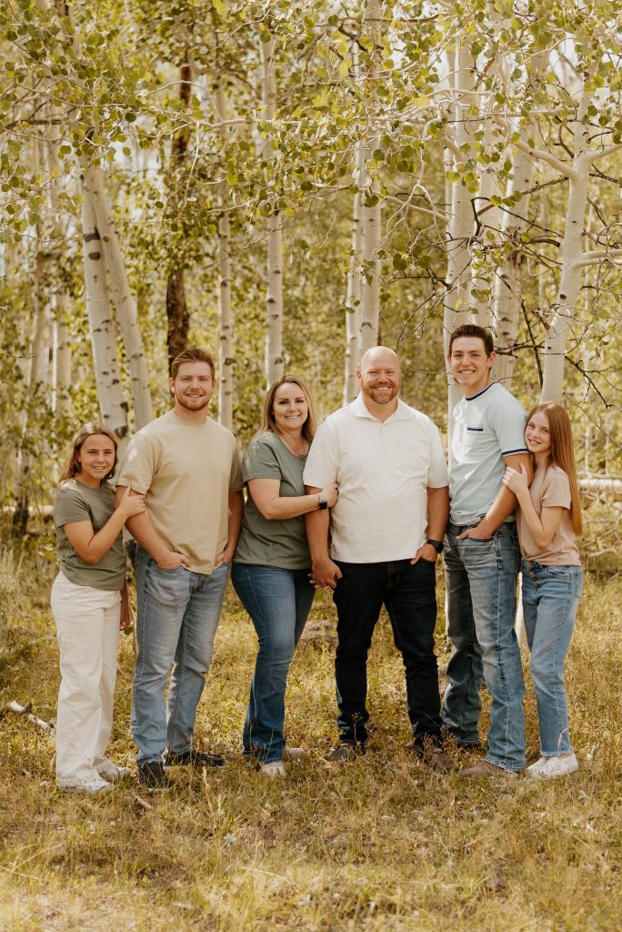 Family portrait in a natural setting, featuring six members smiling together, showcasing a warm atmosphere, surrounded by aspen trees, reflecting a sense of community and support in health insurance.