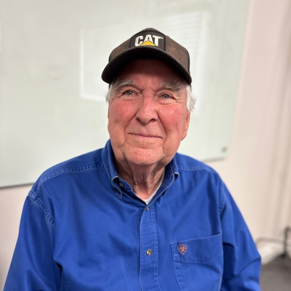 Elderly man in a blue shirt and CAT cap, smiling, representing the supportive team at Optimized Health Plans focused on client care and community impact.